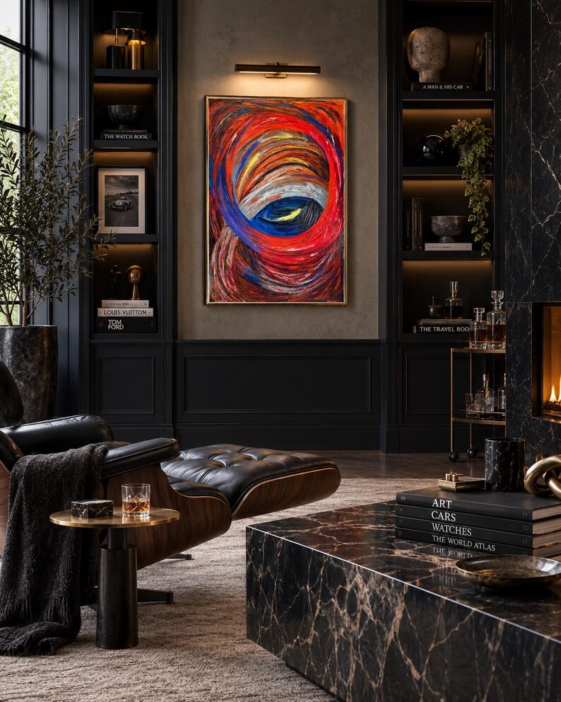 May include: A rectangular abstract painting featuring swirling, thick brushstrokes in vibrant shades of red, orange, and deep blue, framed in a thin gold border and mounted on a dark wall above a black leather lounge chair and a marble coffee table.