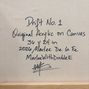 May include: The back of a canvas painting featuring black handwritten text that reads: Drift No. 1, Original Acrylic on Canvas, 36 x 24 in, 2026 Marlee De la Fe, MarleewithDoubleE, and a signature. The canvas is mounted on a light wood frame.