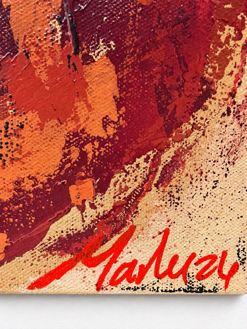 May include: An abstract painting on canvas featuring thick, textured layers of deep red, burnt orange, and gold paint. The surface shows visible brushstrokes and palette knife marks. The signature Maluzy is painted in bright red in the bottom corner.