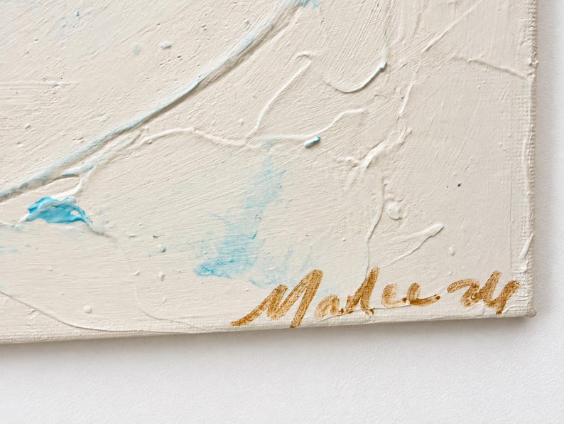 May include: A textured off-white canvas painting featuring raised white paint strokes and subtle light blue accents. The bottom right corner displays a signature in metallic gold cursive script that reads Malee 24.