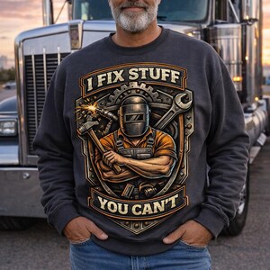 May include: A charcoal gray sweatshirt with the text "I FIX STUFF YOU CAN'T" and a graphic of a welder with tools. The man in the image is wearing blue jeans and standing in front of a semi-truck.