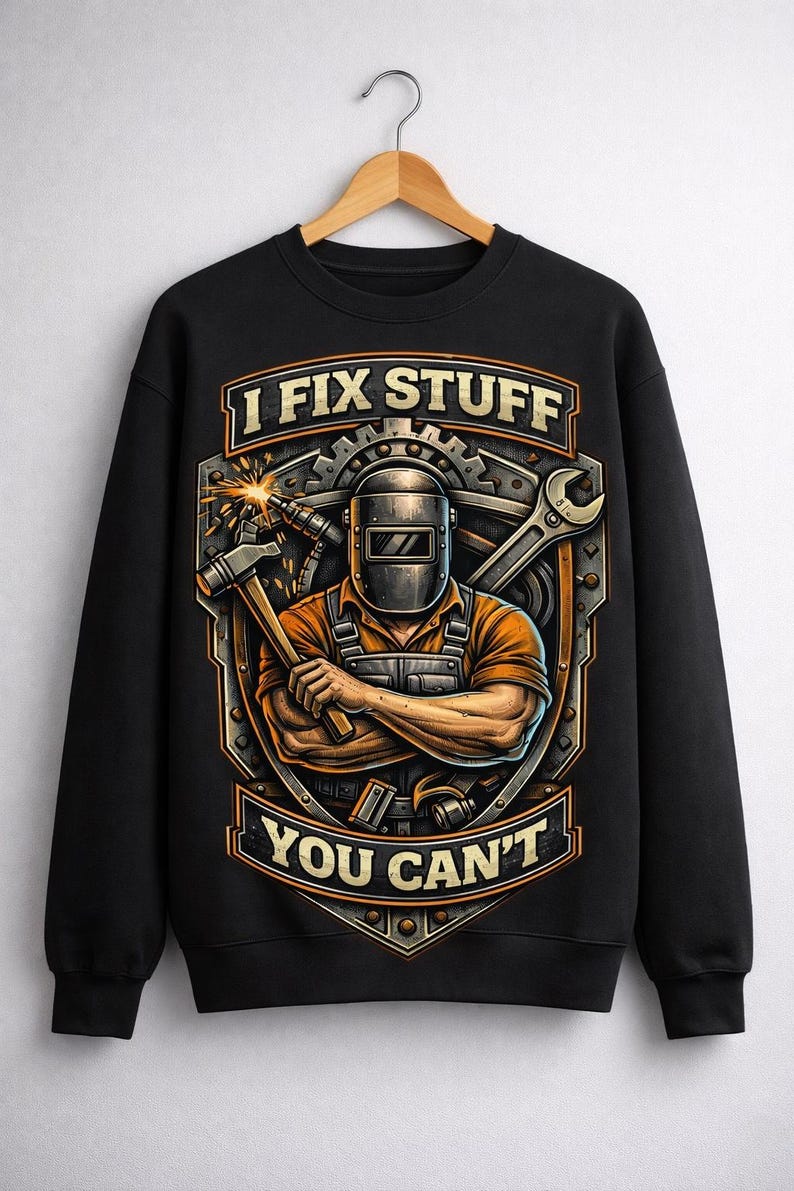 May include: Black sweatshirt with a graphic featuring a welder wearing a mask, holding a hammer, and the text "I FIX STUFF YOU CAN'T". The design includes a wrench and gear elements.