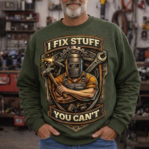May include: Green sweatshirt with the text "I FIX STUFF YOU CAN'T" and a graphic of a welder with tools. The design is in a shield shape with a gear and wrench. The person is wearing blue jeans.