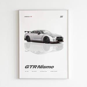 May include: A framed print featuring a silver Nissan GTR Nismo sports car. The car is centered on a white background with its reflection below. The print includes the text "NISSAN" and "GTR Nismo" in a minimalist design.