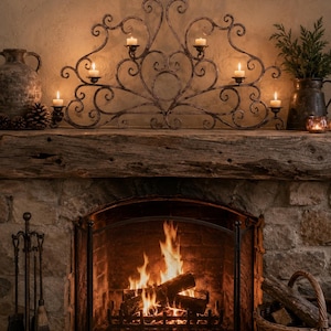 Peut inclure: Une scène de cheminée chaleureuse avec un feu allumé derrière un écran métallique. Au-dessus, un bougeoir décoratif en fer forgé avec des bougies allumées. Une cheminée en bois accueille un vase, des pommes de pin et de la verdure.