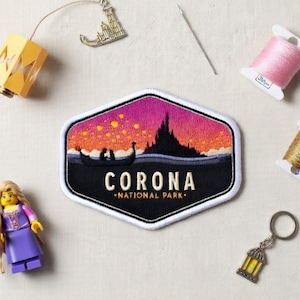 May include: An assortment of craft and collectible items, including a patch with the text "CORONA NATIONAL PARK", a Lego figure, a lantern charm, and spools of thread. The patch features a boat scene with a castle silhouette.