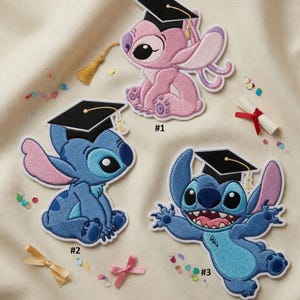 May include: Embroidered patches featuring cartoon characters in graduation caps. The patches include a pink character and two blue characters, each with a unique pose. A rolled diploma with a red ribbon and confetti are also present.
