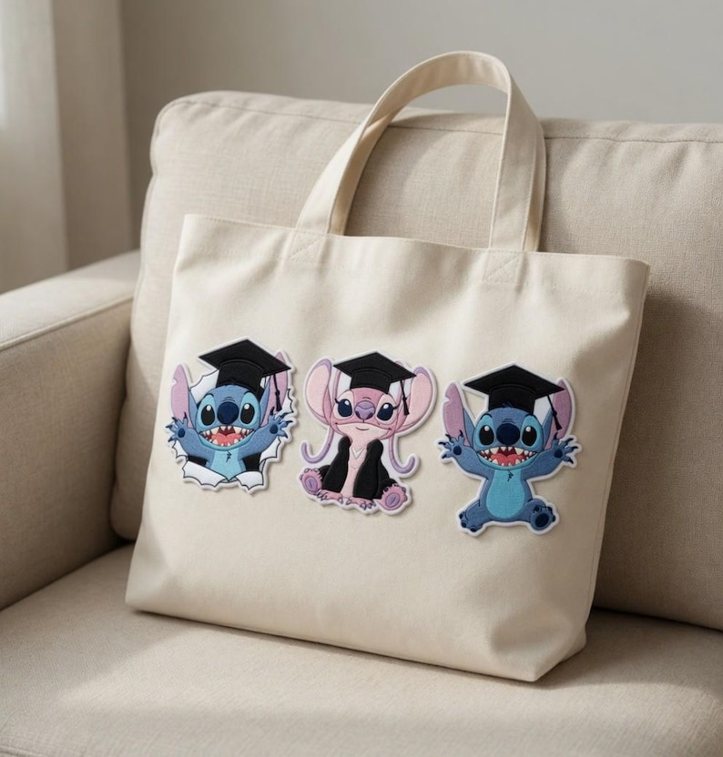 May include: Cream-colored tote bag featuring three cartoon characters wearing graduation caps. The characters are blue and pink, with black graduation caps and gowns. The bag has two handles and is sitting on a beige couch.