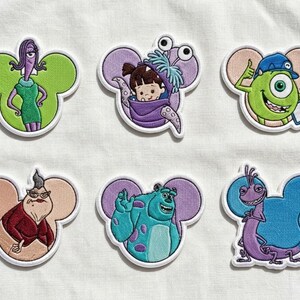 May include: Embroidered patches featuring characters from the animated film "Monsters, Inc." Each patch has a white border and a Mickey Mouse ear shape. Characters include Celia, Boo, Mike Wazowski, Roz, Sulley, and Randall.