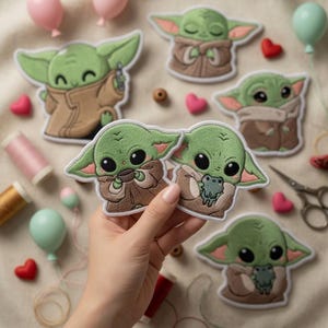 May include: A collection of embroidered patches depicting a green alien character in a brown cloak. The patches are surrounded by sewing supplies, heart-shaped buttons, and balloons. The character is holding a cup, a frog, and a small device.