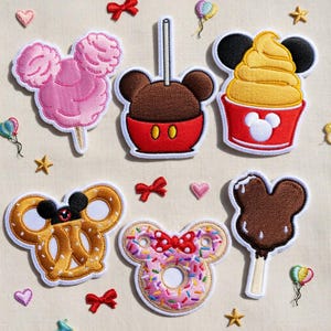 May include: Embroidered patches featuring Mickey Mouse-shaped treats: cotton candy, caramel apple, ice cream, pretzel, donut, and ice cream bar. Each patch has a white border and colorful details, with small bows, hearts, and stars scattered around.