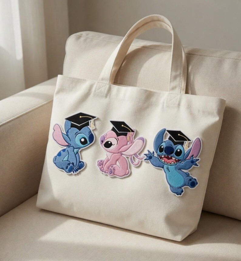 May include: Off-white canvas tote bag featuring three embroidered Stitch characters wearing graduation caps. The characters are in shades of blue and pink, with black caps and gold tassels. The bag has two handles.