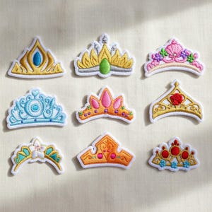 May include: Nine embroidered crown patches in various designs. The crowns feature gold, blue, pink, and orange colors with intricate details. Each patch has a white border, perfect for embellishing clothing or accessories.