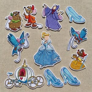 Puede incluir: Colección de parches bordados con personajes y elementos de un cuento de hadas. Incluye Cenicienta, ratones, pájaros, un carruaje y zapatillas de cristal. Los parches son de varios colores, incluyendo azul, amarillo y marrón, con bordes blancos.