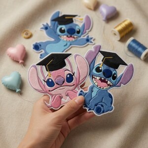 Puede incluir: Parches bordados con el personaje Stitch en varias poses, todos con gorros de graduaci&oacute;n. Los parches son azules y rosas, con gorros negros y borlas doradas. Otros elementos incluyen globos en forma de coraz&oacute;n y carretes de hilo.