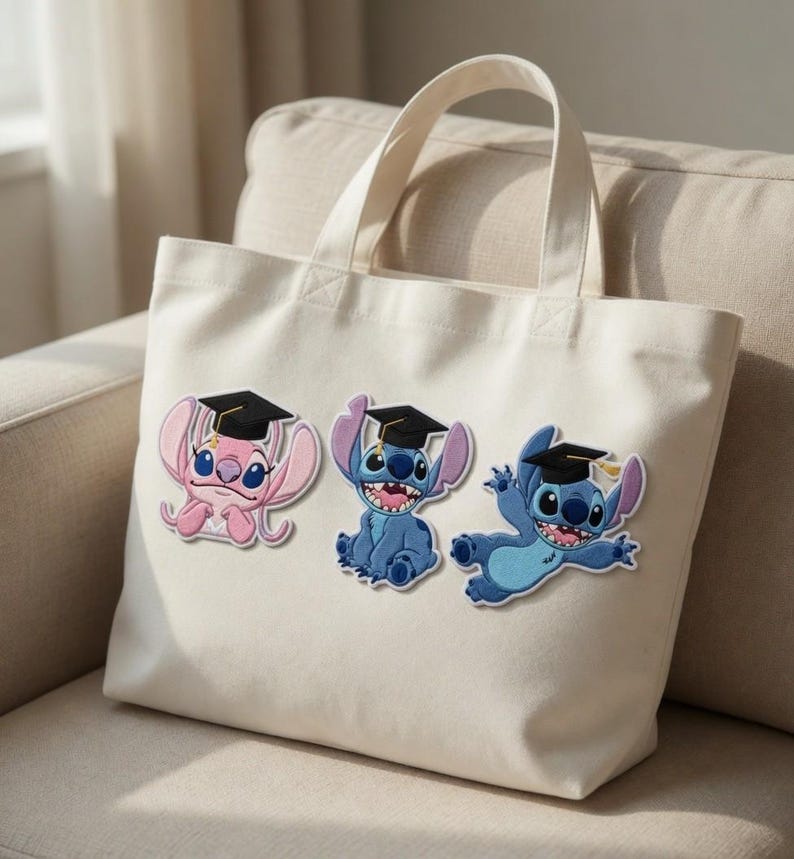 Puede incluir: Un bolso tote de color crema con tres personajes de dibujos animados bordados que llevan gorros de graduaci&oacute;n. Los personajes son en tonos de azul y rosa, con gorras negras y detalles amarillos. El bolso tiene dos asas.