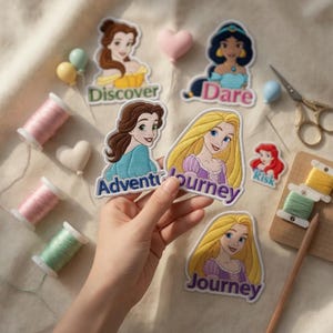 May include: Embroidered patches featuring Disney princesses, including Belle, Jasmine, and Rapunzel. Each patch has a unique design and text, such as "Discover," "Dare," and "Journey." The patches are colorful and detailed, with a white border. Other items include spools of thread and small decorative items.