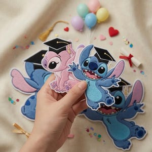 May include: Embroidered patches featuring the characters Stitch and Angel from Lilo & Stitch, wearing graduation caps. The patches are blue and pink, with black caps. Small balloons, confetti, and a diploma are in the background.