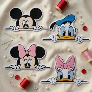 Op de afbeelding: Geborduurde patches met Mickey Mouse, Minnie Mouse, Donald Duck en Daisy Duck. Elk personage wordt afgebeeld terwijl het over een horizontale lijn kijkt. De patches zijn zwart, wit en gekleurd, met een crèmekleurige achtergrond.