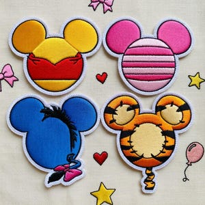 May include: Embroidered patches featuring cartoon character designs. The patches include Mickey Mouse-shaped designs in yellow, red, and pink, along with a blue donkey and an orange tiger. Additional embroidered elements include hearts, stars, and bows.