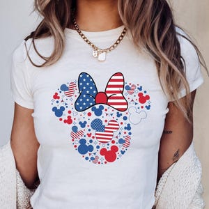 May include: White t-shirt with a Minnie Mouse design in red, white, and blue. The design includes a bow, hearts, and Mickey Mouse silhouettes. The word "WHITE" is in the upper left corner of the image.