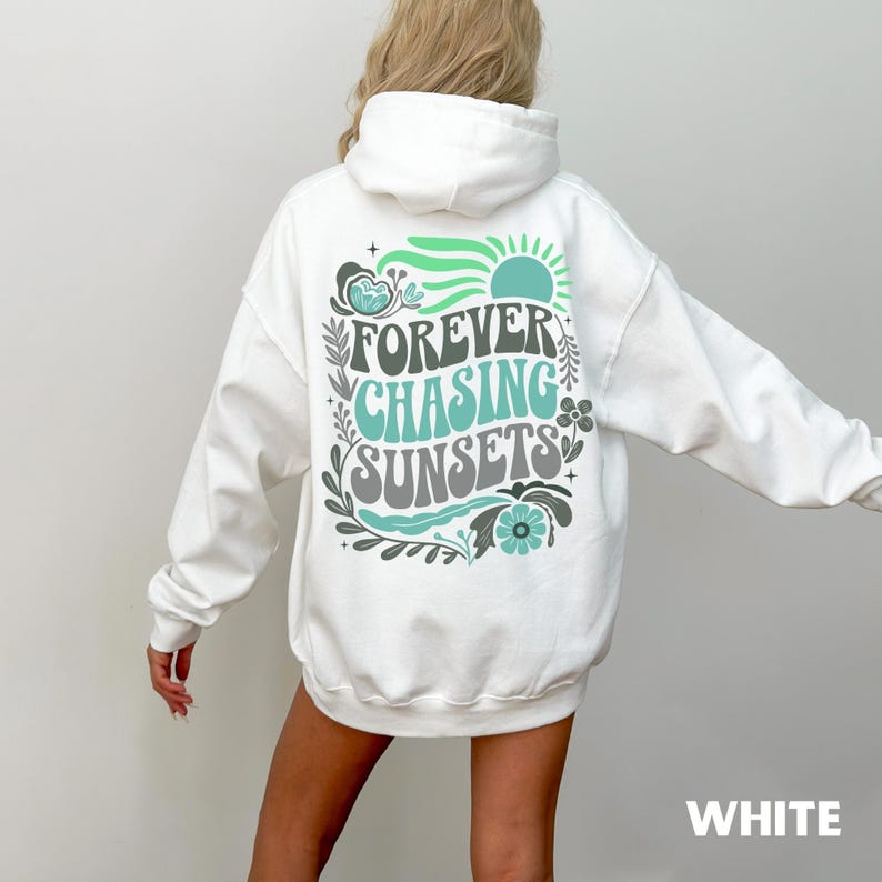 Pode incluir: Moletom branco com a frase "FOREVER CHASING SUNSETS" em um design retr&ocirc;. O gr&aacute;fico inclui um sol, flores e folhas em tons de verde e verde-azulado. A palavra "WHITE" est&aacute; na parte inferior.