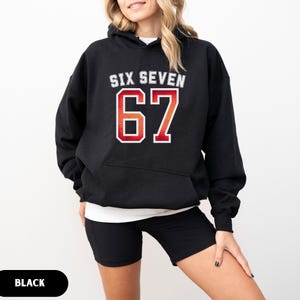 May include: Black hoodie with the text "SIX SEVEN" above the number "67" in a red and orange gradient. The hoodie has a white outline around the text and numbers. The word "BLACK" is in a black oval at the bottom of the image.