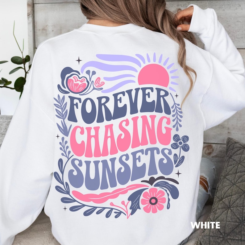 May include: White sweatshirt with the text "FOREVER CHASING SUNSETS" in blue and pink, with floral and sun graphics. The word "WHITE" is printed in the bottom right corner.