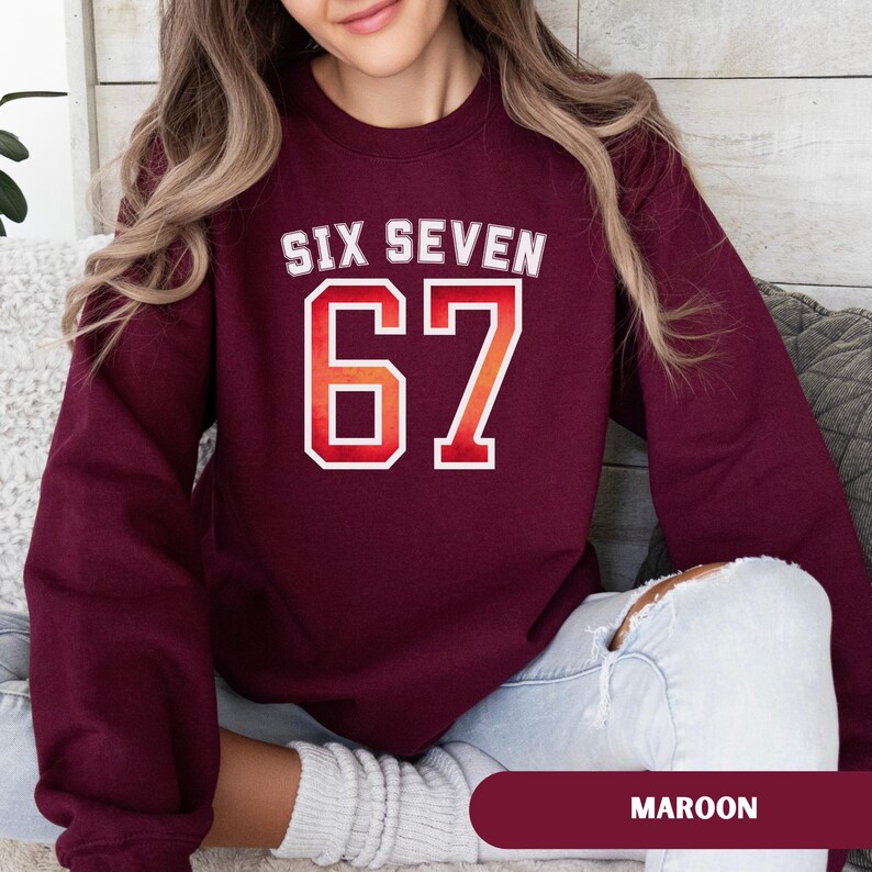 May include: Maroon sweatshirt with the text "SIX SEVEN" above the number "67" in a white and orange gradient design. The word "MAROON" is displayed at the bottom of the image.