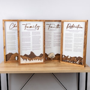 May include: Four framed wooden wall art pieces with text and layered landscape designs. The words "Church", "Family", "Faith", and "Restoration" are displayed. The frames are made of light brown wood, and the background is white.