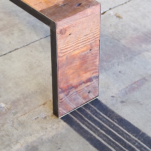 May include: A wooden bench with a metal frame. The bench is made of reclaimed wood and has a rustic look. The bench is sitting on a concrete floor.
