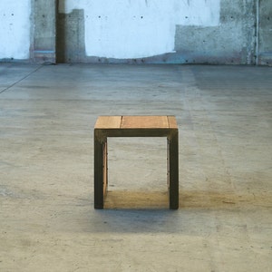 May include: A small wooden table with a dark brown top and black metal legs. The table is sitting on a concrete floor.