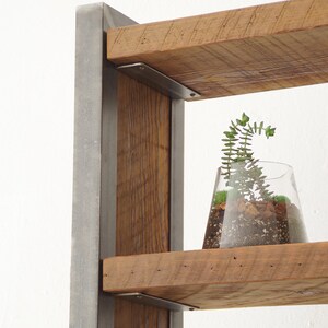 May include: A rustic wooden shelf unit with metal brackets and a small potted plant on one of the shelves. The shelf unit is made of reclaimed wood and has a natural, unfinished look.