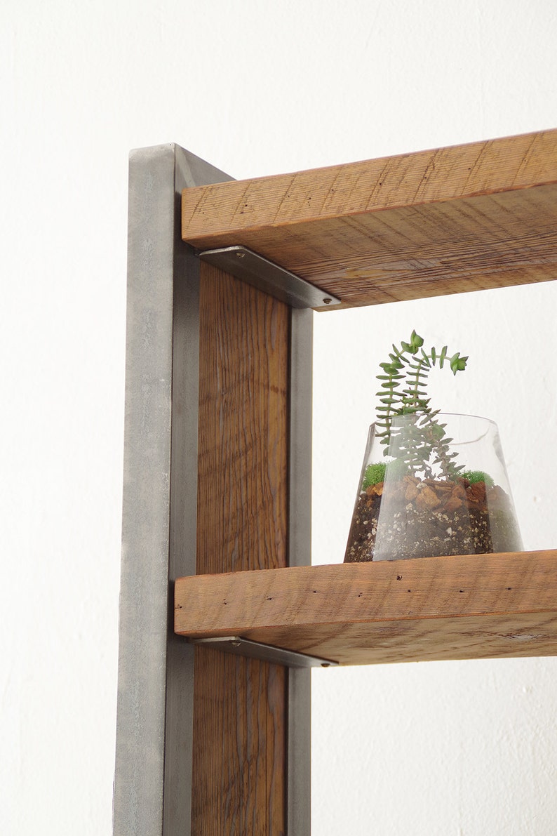 May include: A rustic wooden shelf unit with metal brackets and a small potted plant on one of the shelves. The shelf unit is made of reclaimed wood and has a natural, unfinished look.