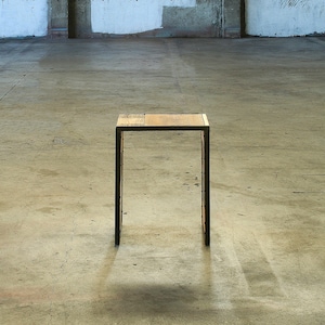 May include: A simple, rectangular wooden table with a black metal frame. The table is standing on a concrete floor.