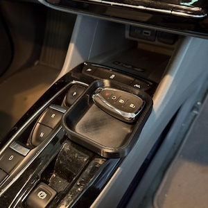 Könnte beinhalten: Ein schwarzes, 3D-gedrucktes Autokonsolenfach mit einem Autoschlüssel darin. Das Fach ist rechteckig und passt in die Mittelkonsole eines Fahrzeugs. Der Schlüssel ist silber und schwarz.