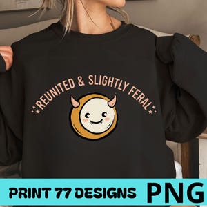 Peut inclure: Un sweat-shirt noir à manches longues avec un motif représentant une créature ronde de couleur crème, dotée de petites cornes et d'un visage souriant. Le texte REUNITED & SLIGHTLY FERAL est imprimé en arc rose clair au-dessus de la créature.