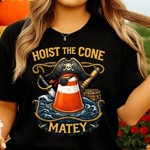 Op de afbeelding: Zwart T-shirt met een piratenthema. Het ontwerp toont een verkeerskegel met een ooglapje en piratenhoed, met de tekst "HOIST THE CONE MATEY". Een zwaard, een telescoop en een schatkist zijn ook inbegrepen.