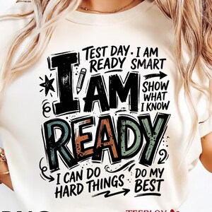 Puede incluir: Camiseta color crema con el texto "Test Day. I am ready smart. I am ready. I can do hard things. Do my best." El diseño incluye un lápiz, una estrella y flechas. Es una prenda informal.
