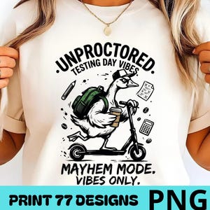 Peut inclure: T-shirt crème avec un dessin d'oie sur un scooter, portant un chapeau et un sac à dos, tenant une tasse de café. Le texte dit "Unproctored Testing Day Vibes" et "Mayhem Mode. Vibes Only."