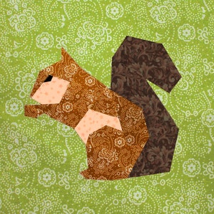 May include: A brown and tan squirrel with a brown tail, made from fabric with a paisley pattern, on a green background with white floral designs.