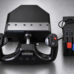 May include: A black flight yoke system with a central digital display, multiple buttons, and a toggle switch. Beside it sits a black throttle quadrant featuring three vertical levers with red and blue knobs, connected by a black cable.