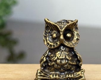 May include: A small, detailed brass owl figurine. The owl has large eyes and textured feathers, with a slightly aged appearance. It is standing on a small base, and the overall design is intricate and decorative.