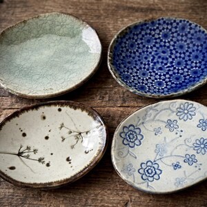 May include: Four ceramic plates with unique designs. One is pale green with a crackle pattern, another has a blue floral pattern, a third features a botanical design, and the last has a blue and white floral pattern.
