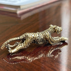 Op de afbeelding: Gedetailleerd metalen tijgerbeeldje in een rennende pose. De tijger is goud- en zilverkleurig, met ingewikkelde details op zijn lichaam. Het beeldje is ongeveer 10 cm lang en wordt getoond op een reflecterend oppervlak.