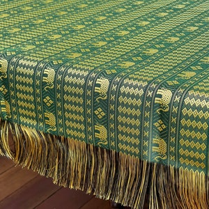 May include: Green and gold table runner with a repeating pattern of elephants and geometric shapes. The runner has a fringe border.