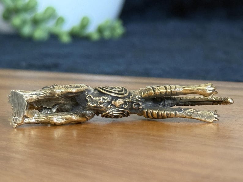 Op de afbeelding: Een gedetailleerd, goudkleurig beeldje van een mythisch wezen, mogelijk een draak of een soortgelijk wezen. De sculptuur ligt, met ingewikkelde details zichtbaar op het lichaam, inclusief schubben en sierlijke patronen. Het beeldje staat op een houten oppervlak.