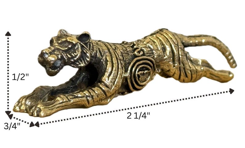 Op de afbeelding: Een bronzen tijgerbeeldje in een springhouding. De sculptuur is 5,7 cm lang, 1,9 cm breed en 1,3 cm hoog. De tijger heeft gedetailleerde strepen en gezichtskenmerken, met een cirkelvormig ontwerp aan de zijkant.