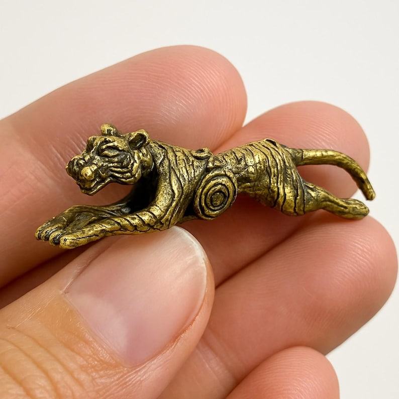 Op de afbeelding: Een kleine, gedetailleerde messing tijgerfiguur in een rennende pose. De tijger heeft ge&euml;tste strepen en een textuur, met zijn kop en staart omhoog. Het beeldje heeft een goudbruine kleur.