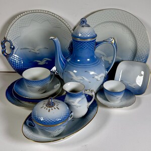 May include: A complete blue and white porcelain tea set with a seagull motif. The set includes a teapot, cups, saucers, plates, a creamer, a sugar bowl, and a serving platter. The set has gold trim.